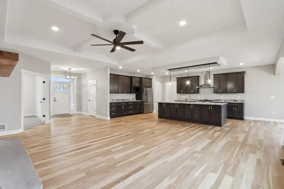 Open kitchen with a dark shaker island, white oak floors and a coffered ceiling running through to the entry