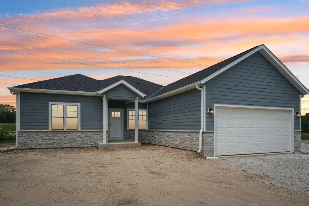 New ranch home with blue lap siding and stone skirt at sunset, built by G&A Construction