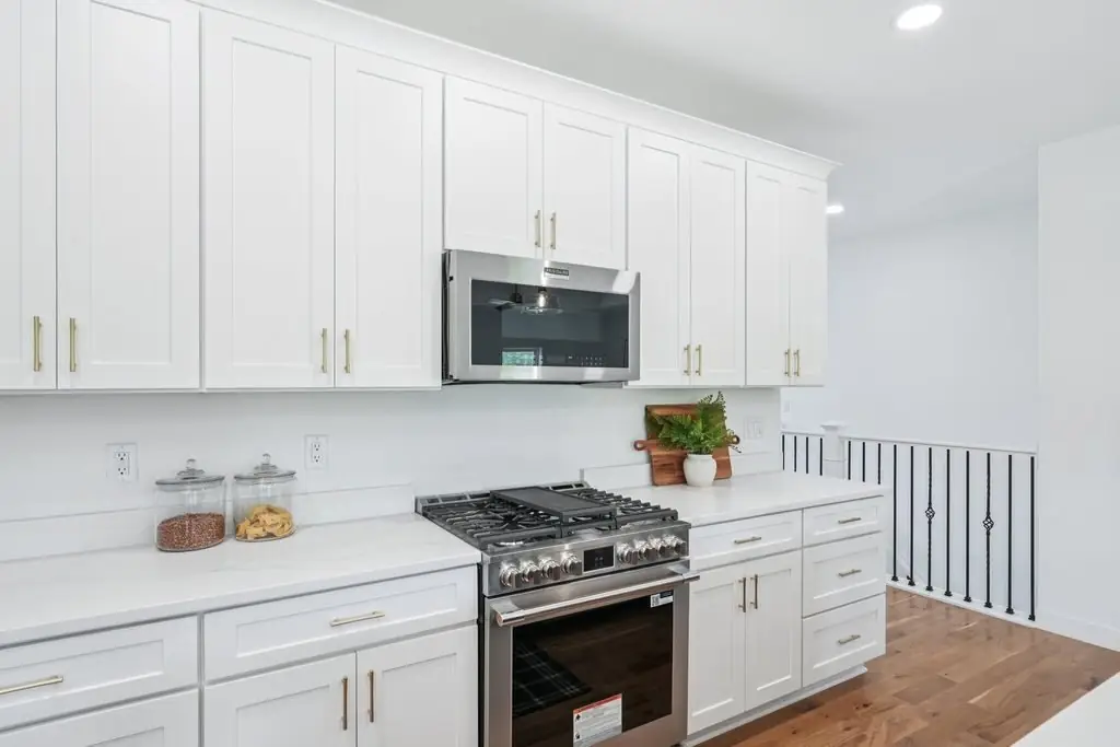 Range wall with white shaker cabinets and brass hardware, beside the stair rail
